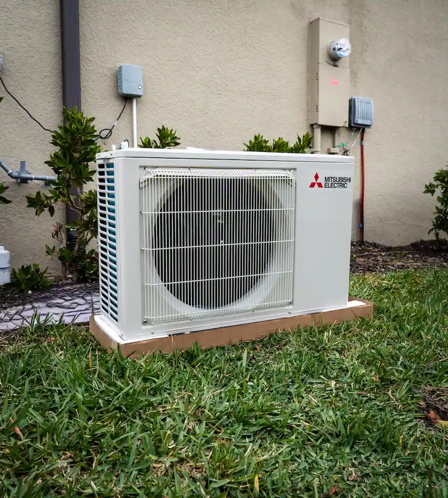 A brand new Mitsubishi condenser unit for a mini-split sitting outside a home getting ready to be installed.