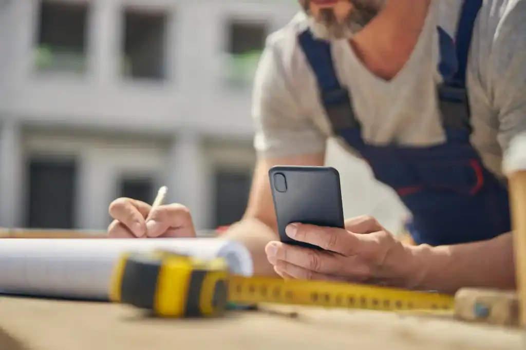 Closeup of a worker reviewing blueprints while using a cellphone.